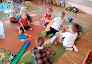 Dzieci bawią się na dywanie torami samochodowymi.