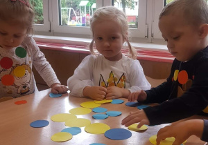 Przedszkolaki bawią się kropkami wyciętymi z kartonu.
