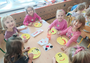 Dzieci przy stoliku malują farbami buźki z uśmiechem
