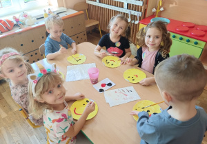 Dzieci przy stoliku malują farbami buźki z uśmiechem