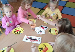 Dzieci przy stoliku malują farbami buźki z uśmiechem
