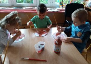 Przedszkolaki wykonują pracę plastyczną- malują sylwetę jeża farbami.