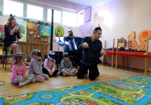 Wokalistka śpiewa piosenkę, a Pan Maciek z dziewczynkami w maskach kotów siedzą na scenie.