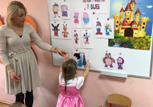 Dziewczynka pokazuje na tablicy postacie bajkowe.