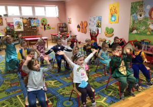 Dzieci siedzą na krzesełkach i klaszczą w dłonie.