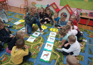 Dzieci wspólnie z nauczycielką przeliczają obrazki przedstawiające zwierzęta.