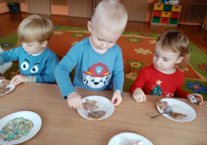 Dzieci ozdabiają pierniki posypką i piankami.