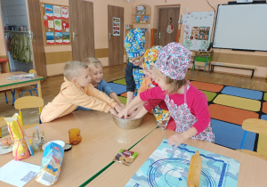 Dzieci zagniatają ciasto na pierniki w misce.