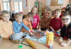 Dzieci razem z panią foremkami wykrawają w cieście pierniki