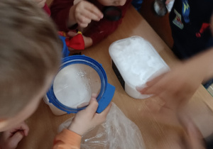 Dzieci obserwują śnieg przyniesiony do przedszkola przez lupy