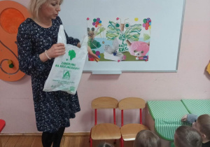 Nauczycielka pokazuje dzieciom plansze edukacyjne dotyczące ekologicznych zachowań.