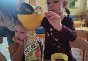Dziewczynka wsypuje ziarna do butelki.