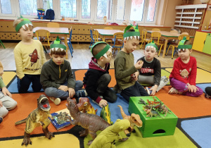 Dzieci na dywanie oglądają figurki dinozaurów