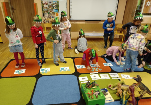 Dzieci na dywanie rozwiązują zadania o dinozaurach