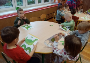 Dzieci tworzą figury dinozaury z gotowych kart pracy.