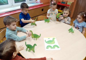 Przedszkolaki bawią się wykonanymi dinozaurami.
