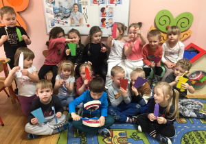 Dzieci na tle tablicy demonstracyjnej pokazuję przybory do mycia zębów.