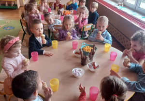 Przedszkolaki jedzą słodki poczęstunek.