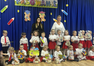 Zdjęcie pamiątkowe - grupa dzieci z nauczycielkami stoją na niebieskim tle z dekoracją