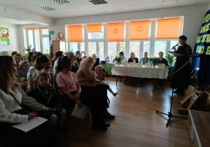 Widownia - dorośli i dzieci -siedzą na krzesłach, na drugim planie Jury siedząca za stołem
