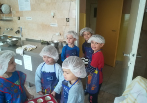 Dzieci wnoszące do kuchni babeczki do upieczenia.