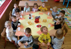 Dzieci siedzą przy zastawionym stoliku pozują do zdjęcia