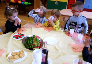Dzieci jedzą , pija przy stoliku.