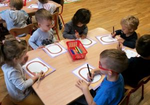 Dzieci przy stole malują kredkami koszyk, naklejają warzywa.