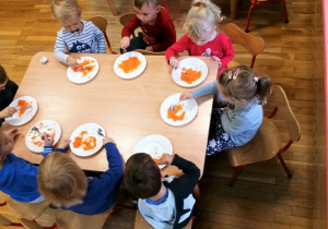 Dzieci siedzą przy stole jedzą marchewkowa surówkę.
