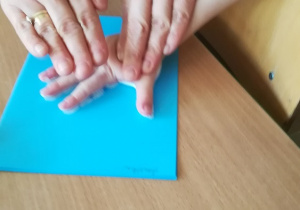 Odbijanie dłoni pomalowanej farbą na niebieskiej kartce