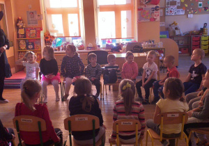 Dzieci siedzą na krzesełkach i słuchają nauczycielki przebranej za wróżkę