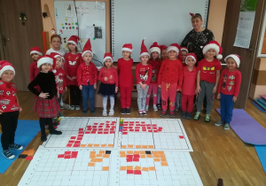 Obrazek Mikołaja z kolorowych karteczek na macie kodującej i z tyłu grupa dzieci