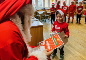 Mikołaj rozdaje dzieciom prezent i certyfikat grzecznego dziecka