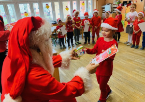 Mikołaj rozdaje dzieciom prezent i certyfikat grzecznego dziecka