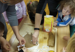 Pani Beatka pomaga maluszkom wyciskać foremkami ciasteczkowe pierniki