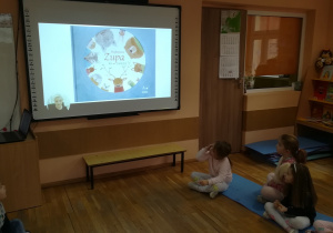 Dzieci słuchają i oglądają na tablicy multimedialnej bajkę.