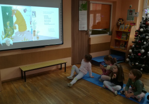 Dzieci słuchają i oglądają na tablicy multimedialnej bajkę.