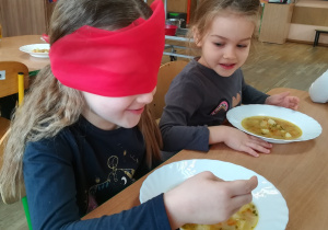 Dziewczynka z zasłoniętymi oczami czerwoną chustką rozpoznaje zupę po smaku.
