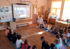 Przedszkolaki z grupy V oglądają i słuchają opowiadania czytanego przez gości zaproszonych do MBP.