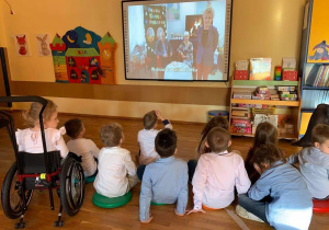 Przedszkolaki z grupy IV oglądają i słuchają opowiadania czytanego przez gości zaproszonych do MBP.