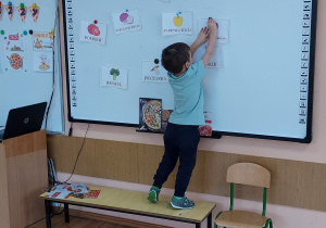 Chłopiec przyczepia na tablicy obrazki przedstawiające składniki pizzy