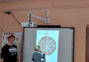 Chłopiec liczy na tablicy multimedialnej na ile części jest pokrojona pizza