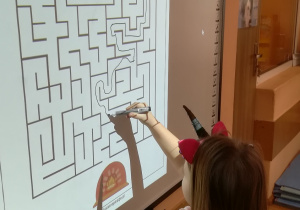 Dziewczynka rozwiązuje labirynt na tablicy multimedialnej