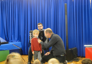 Pan z akordeonem, mały chłopiec i pan trzymający mu mikrofon.