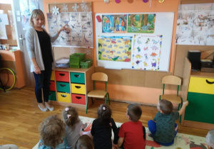 Nauczycielka pokazuje na ilustracji różne dinozaury.