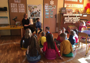 Nauczycielka prezentuje dzieciom z grupy IV książki i ilustracje o dinozaurach.