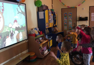 Dzieci wykonują ćwiczenia ruchowe wyświetlane na tablicy multimedialnej.