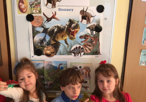 Dzieci przy tablicy pokazują figurki dinozaurów.