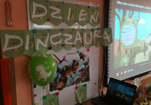 Tablica z przypiętymi literami "Dzień dinozaura" i obrazek z dinozaurami