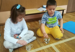 Dzieci mieszają łyżeczkami w szklankach z wodą węgiel i sól.